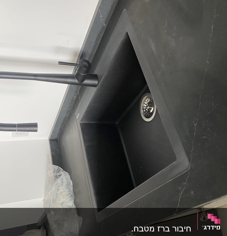 כיור שחור עם ברז מעוקל על משטח עבודה